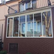 Zabudowa balkonu płytkami w kolorze bordowym i szklaną obudową z oknami.